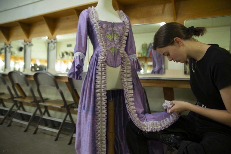 马德斯莱顿 bends over to look at the hemline of a purple costume.