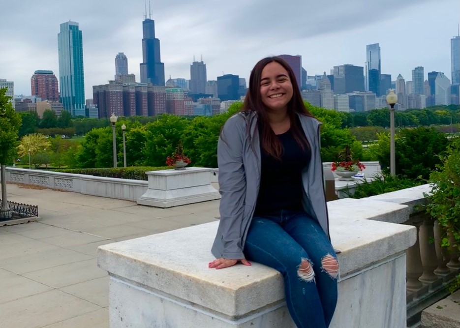 student Steph任何 Pichola sitting on a stone railing with the background of the Milwaukee skyline