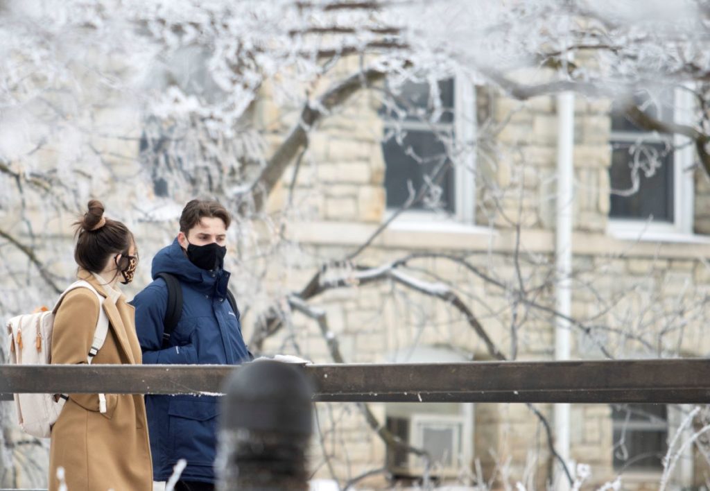 Two students walking across campus and in the background trees covered in snow