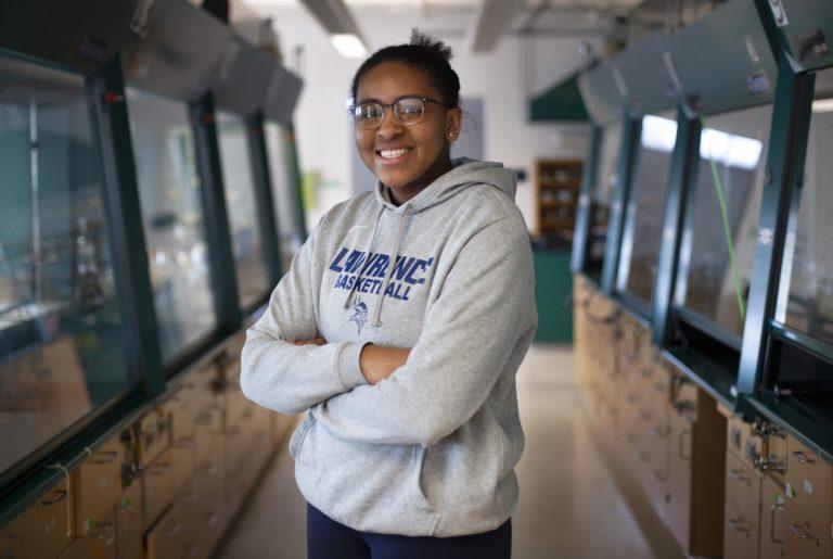 肯尼亚伯爵, wearing a grey Lawrence basketball sweatshirt, stands with her arms crossed and smiles at the camera.