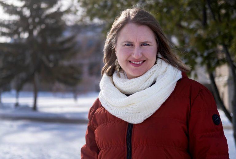 Celia Barnes, wearing a red coat and white scarf, smiles at the camera.