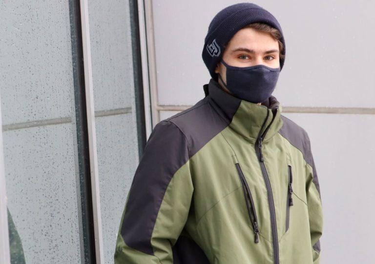 Justin Williamson, wearing a navy blue mask and green jacket, looks at the camera.