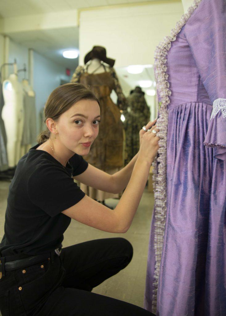 马德斯莱顿 adjusts the stitching on an old-fashioned purple gown.