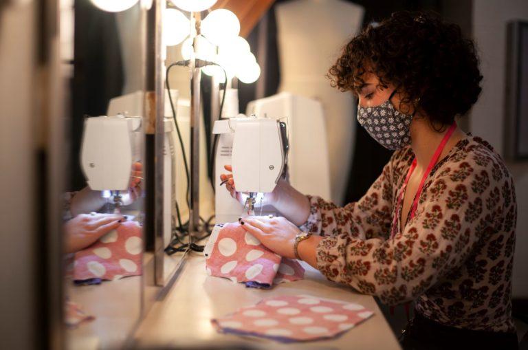 玛吉McGlenn, wearing a polka-dot mask, uses a sewing machine to work on pink polka-dot fabric..