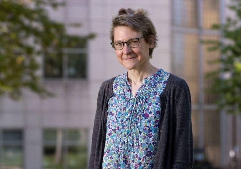 Marcia Bjornerud, wearing a blue floral shirt and a grey cardigan, smiles at the camera.