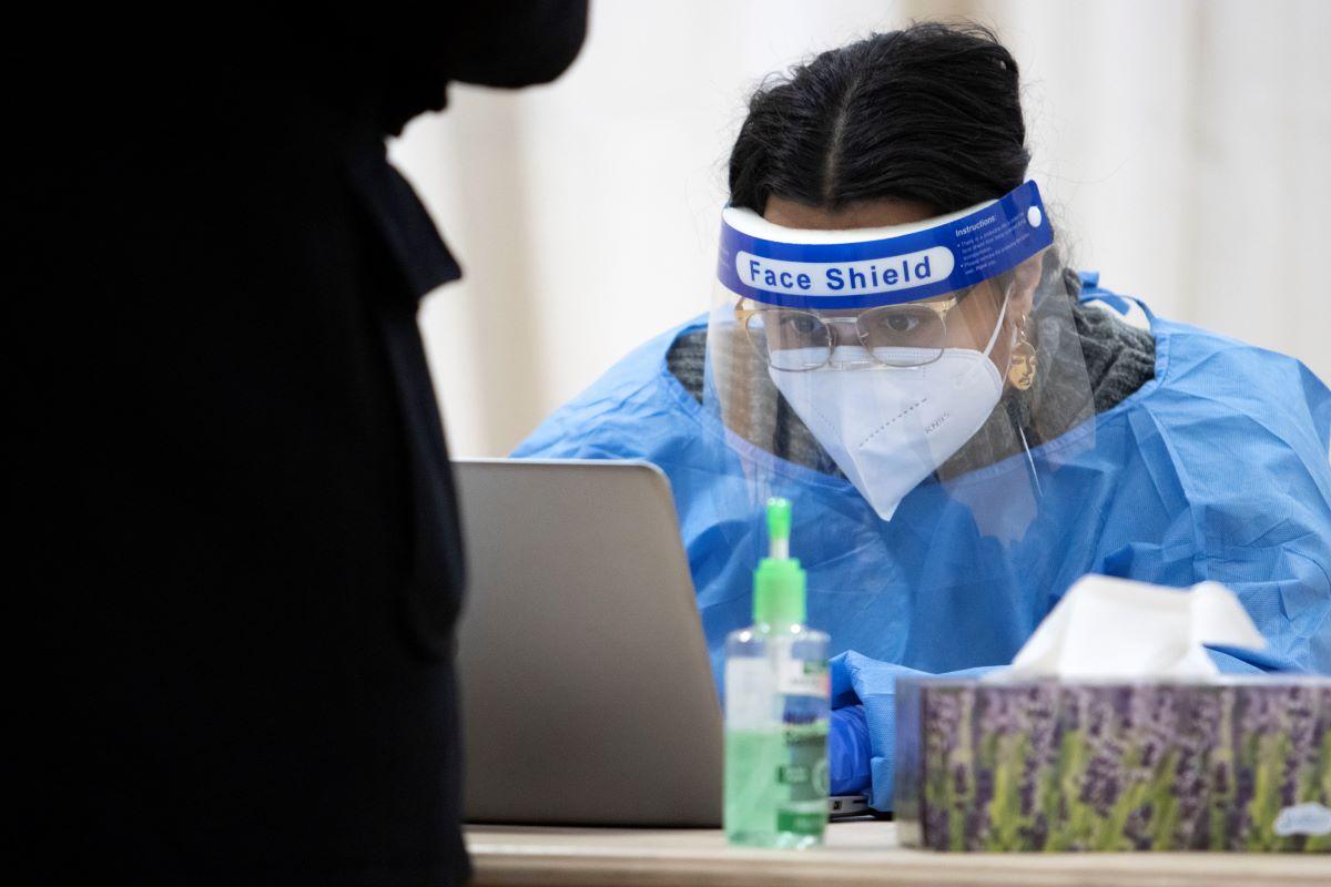 student worker, using protective gear, signs people up in the computer for their COVID-19 test