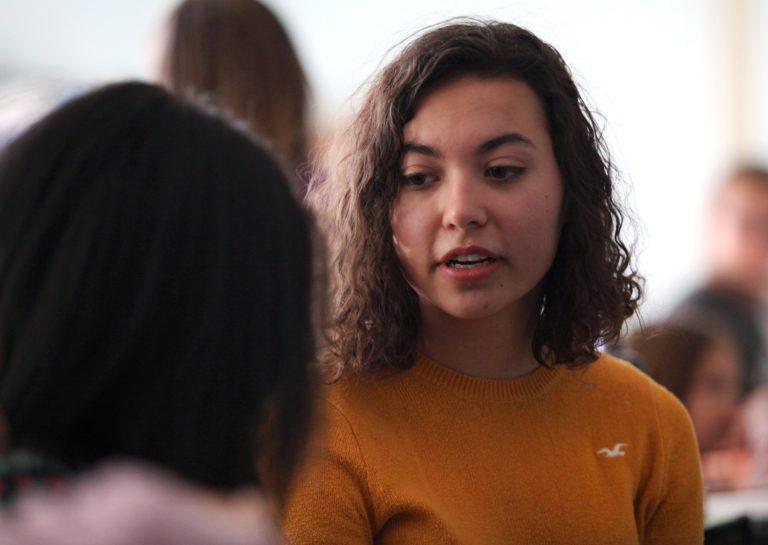 苏菲Dion-Kirschner, wearing a yellow sweater, speaks to a dark-haired girl.
