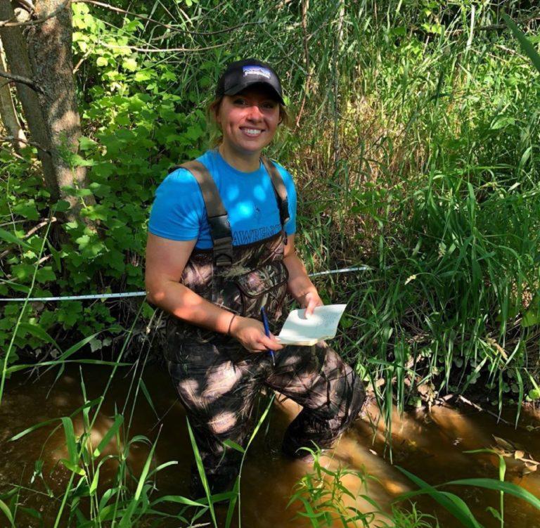 夏天Kopitzke squats in a creek, surrounded by greenery.