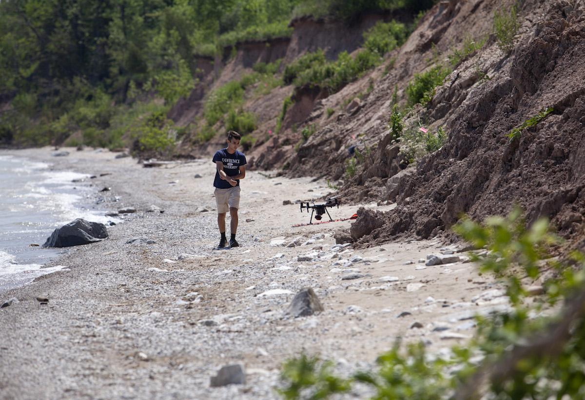 Student walking along the shore of Lake Michigan while using a drone 