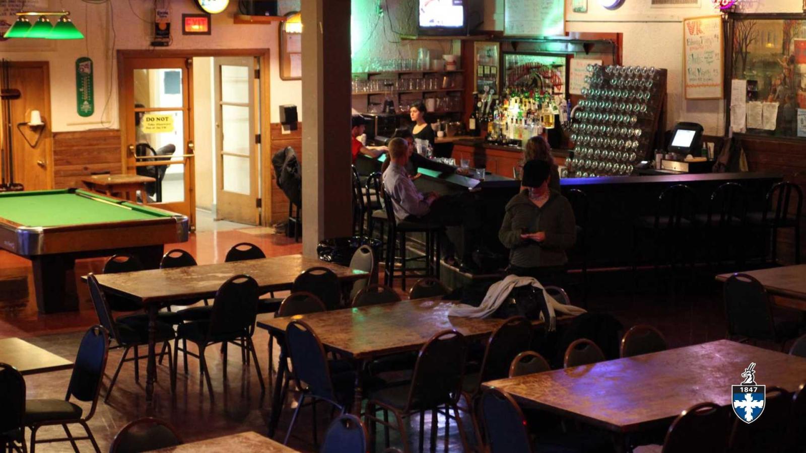 Students sitting around bar waiting for drinks in mostly empty bar.