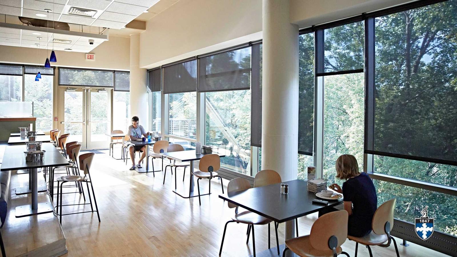 Students sitting near window in cafeteria eating.