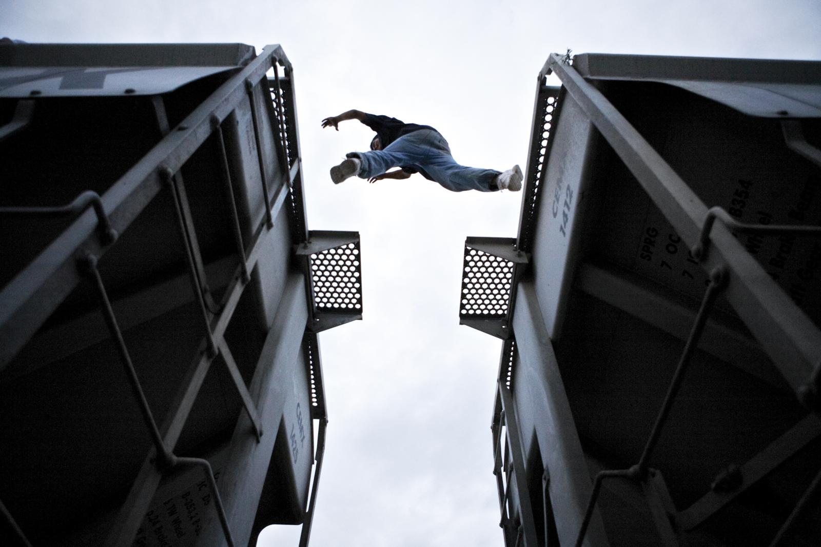 Man jumping between two train cars shot from below.