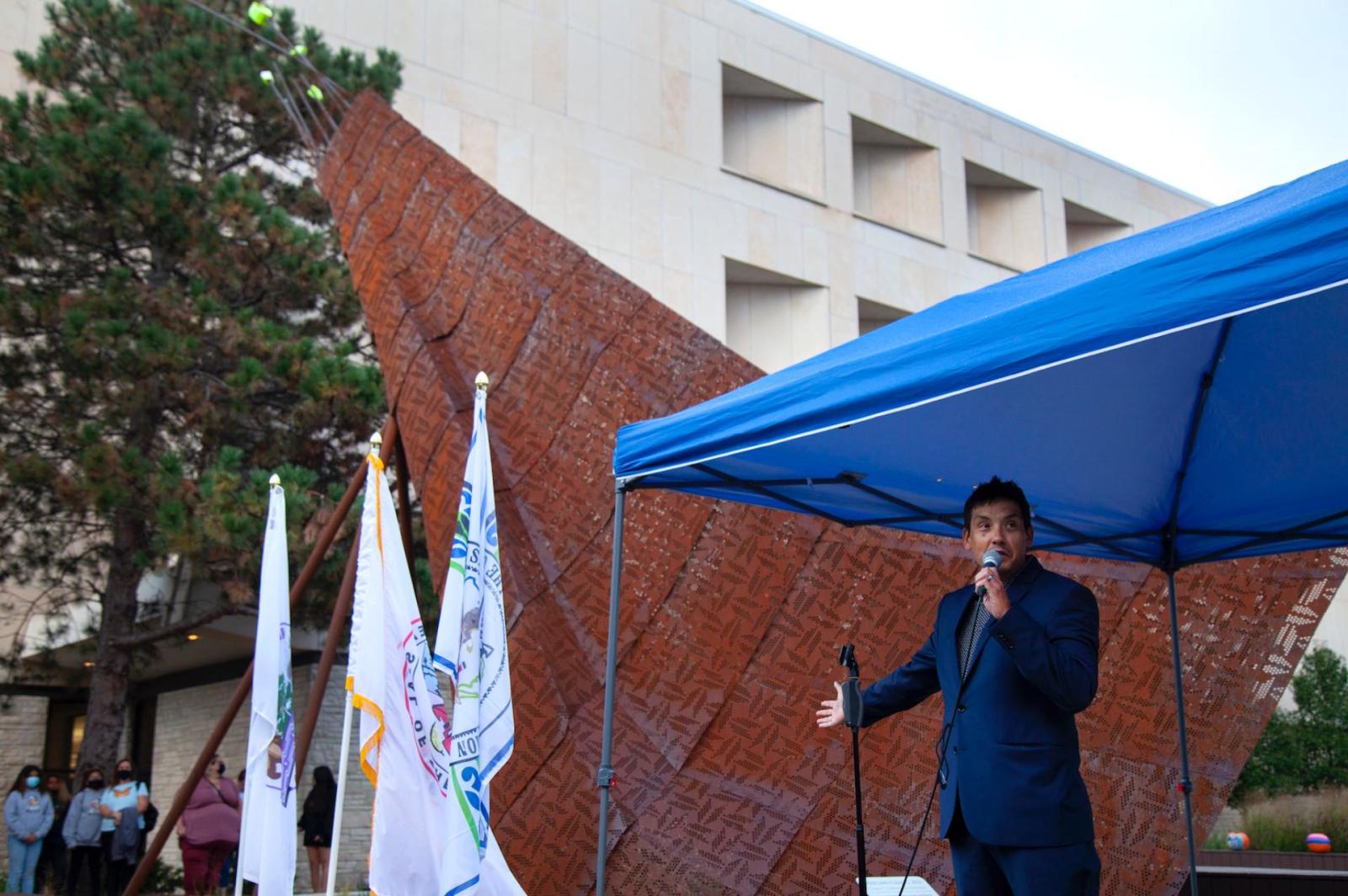 Architect Chris Cornelius speaks under a tent next to the crane sculpture he designed during Lawrence's sixth annual Indigenous Peoples' Day Celebration.