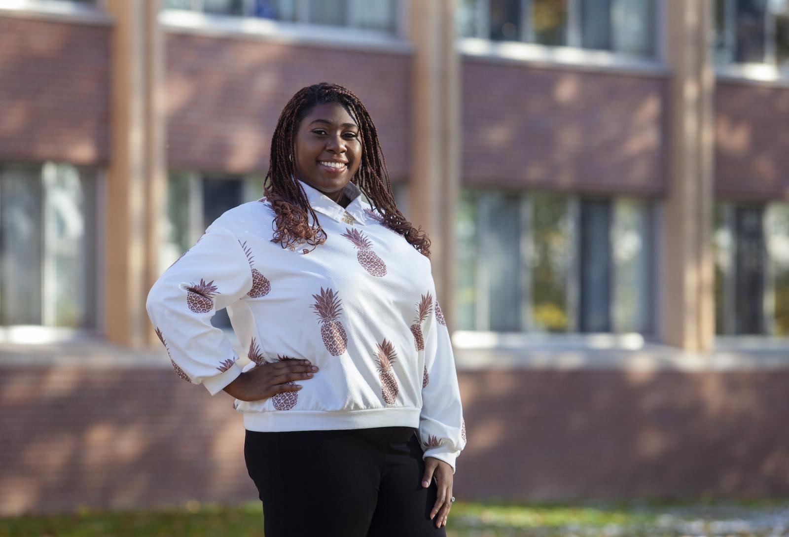 Ladora Thomas poses in front of a brick building, wearing a shirt with a pineapple pattern.