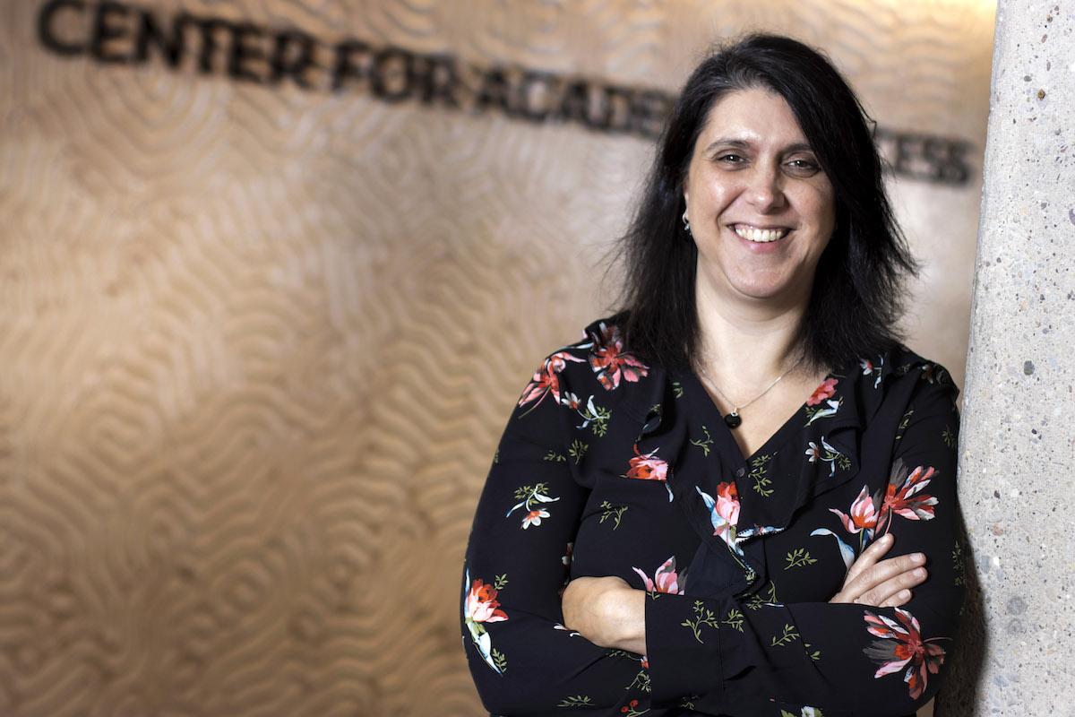 Monita Mohammadian Gray, wearing a floral patterned shirt, poses against a wall in the Center for Academic Success.