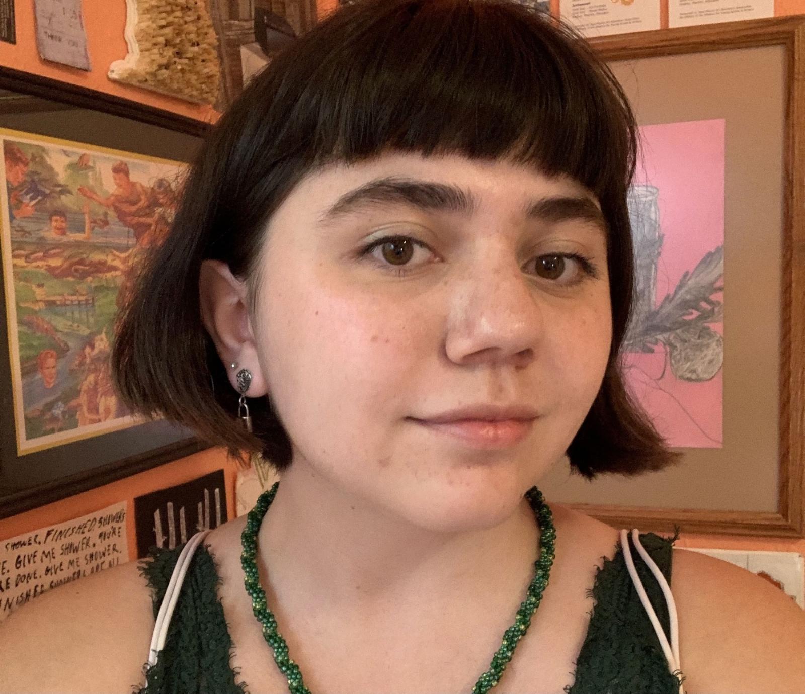 Emma Goodman, a student seeking an art degree from Lawrence, poses for profile pic in front of her art her art displayed on the wall in the background.