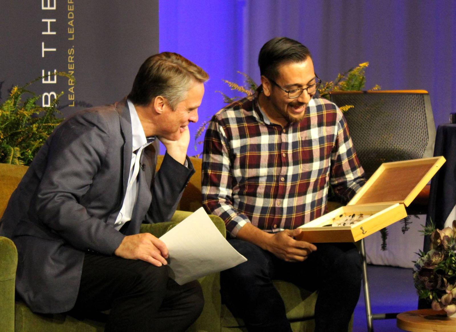 Terry Moran leans in look inside Israel Del Toro's box as they're both seated in plush armchairs.