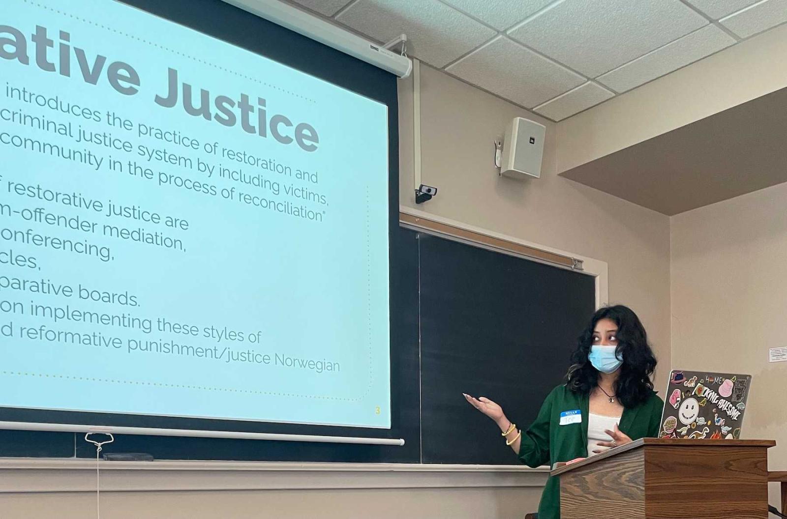 Tee Karki points to her work on a big screen during her Harrison Symposium presentation.