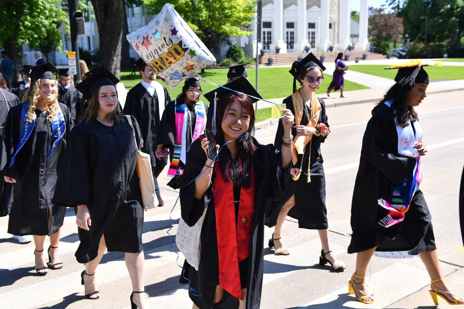A graduate holds a Congrats Grad balloon as she and other graduates walk across 大学 Avenue during the 2022 Commencement.