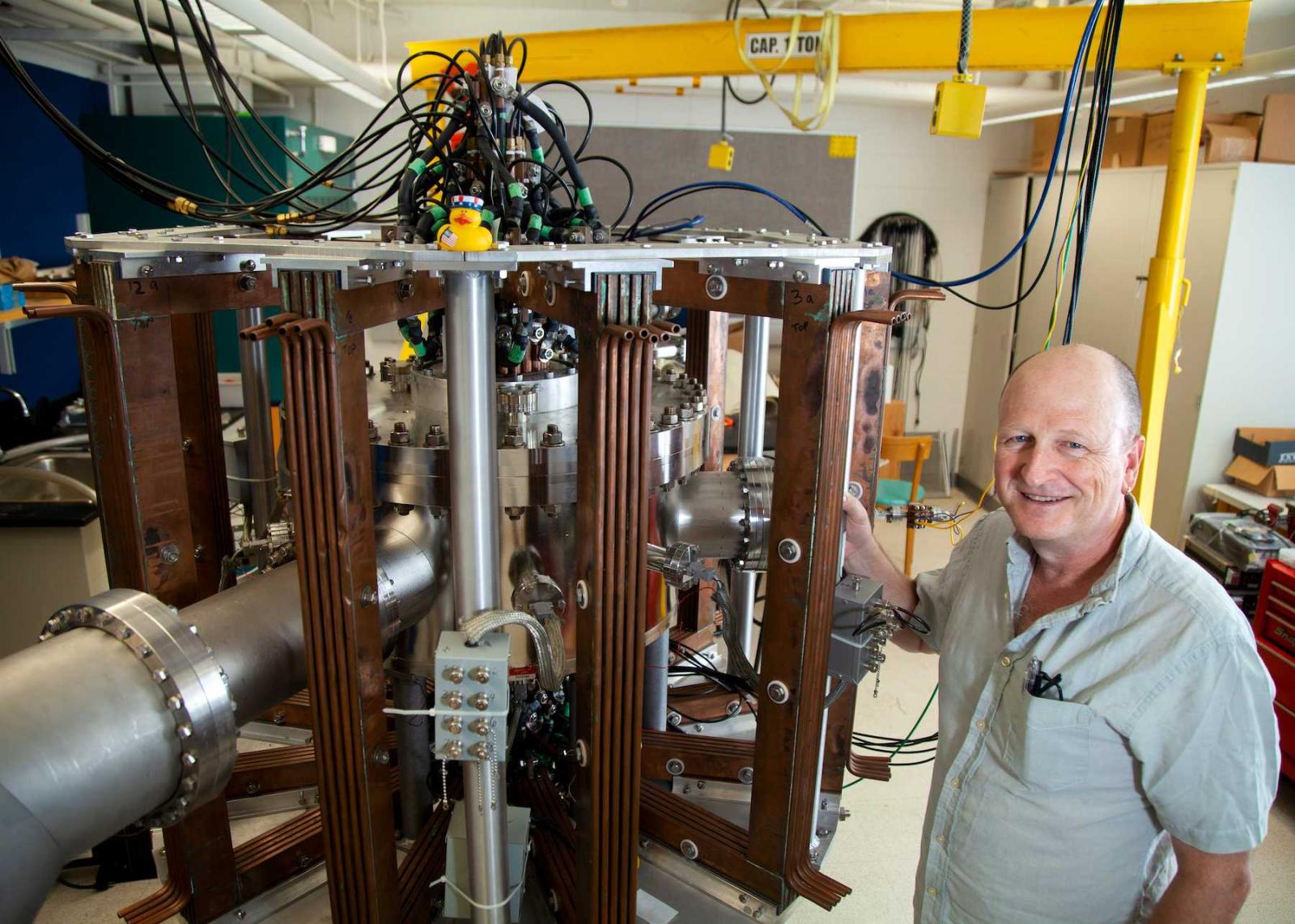 Physics professor Matthew Stoneking poses for a photo with research equipment in his lab in Youngchild Hall.