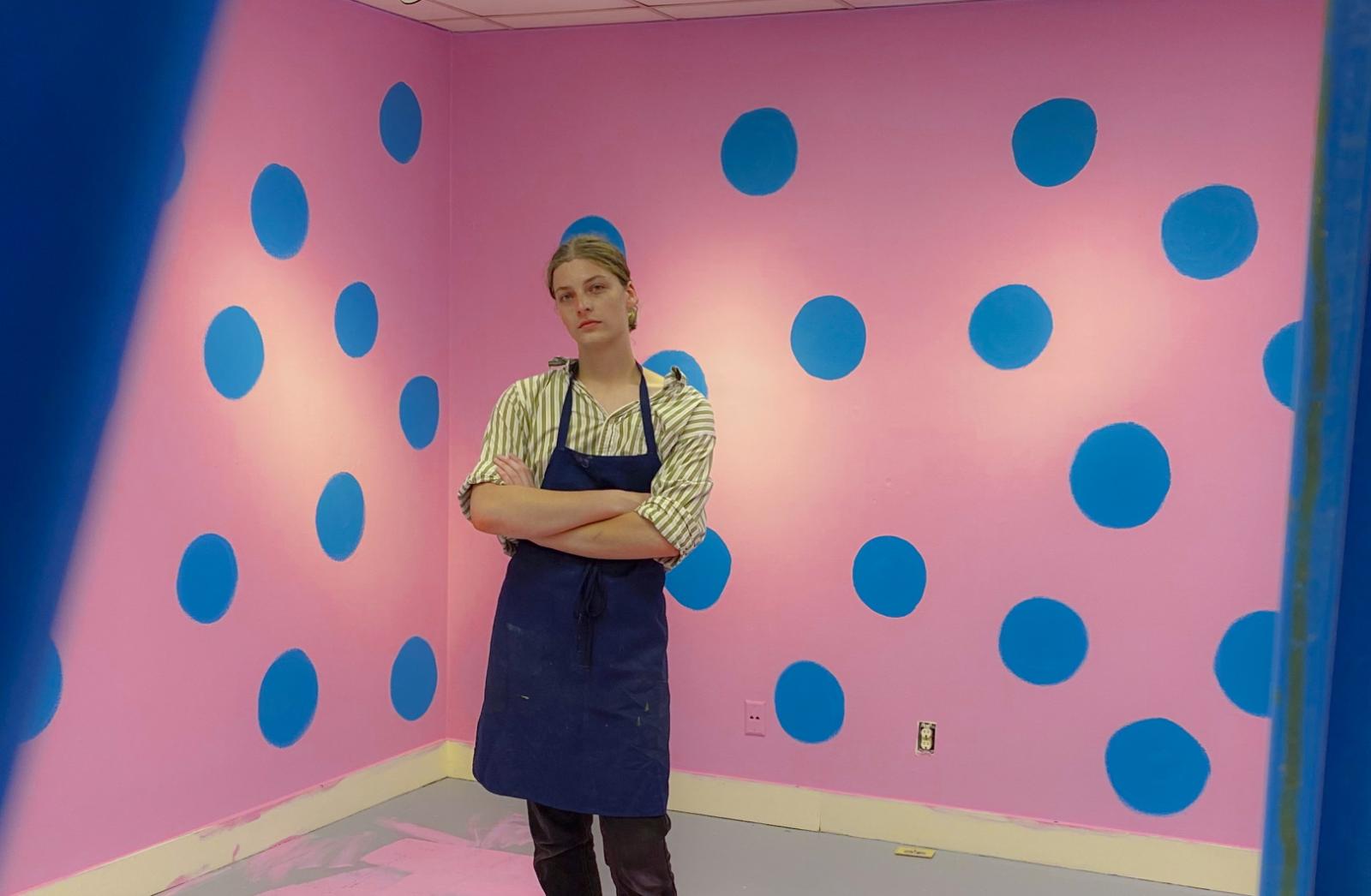 Charlie Wetzel poses for a photo in the middle of a pink and blue art installation.
