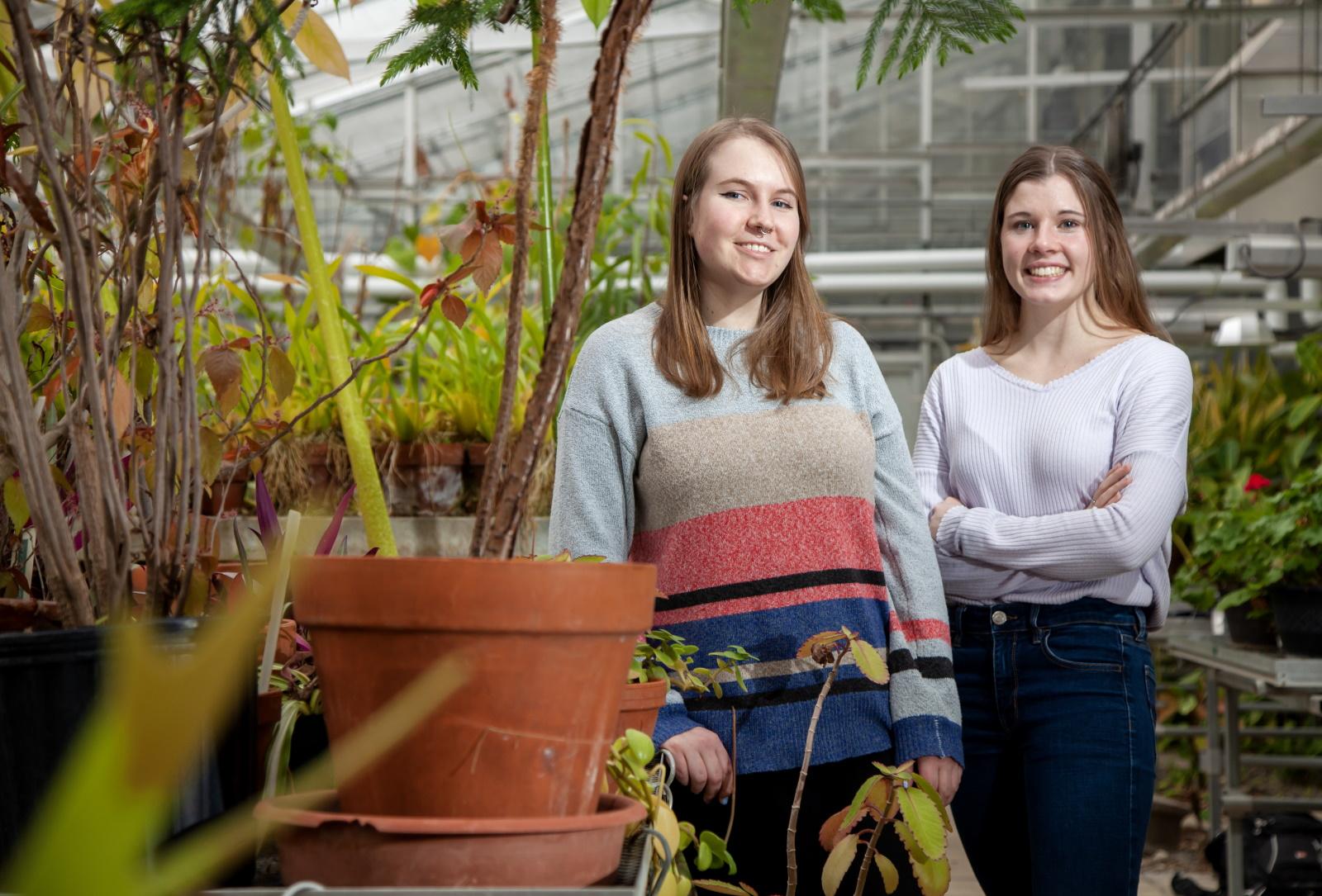 Amber Newman and Madeline Taylor stand in the greenhouse in Briggs Hall.