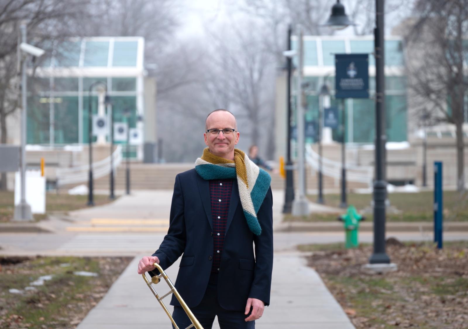 Tim Albright poses with his trombone on the sidewalk of Main Hall Green.