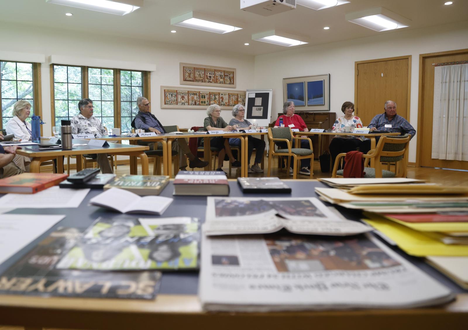 a table in the foreground with paper and students in the background