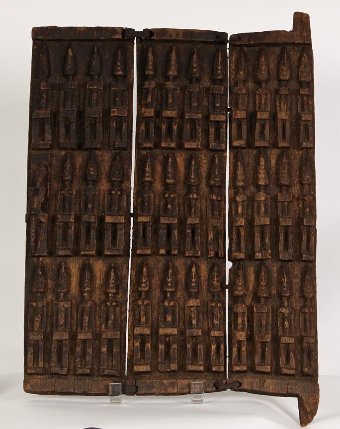 a brown wooden door divided vertically in three parts with stylized human figures in rows carved onto them.