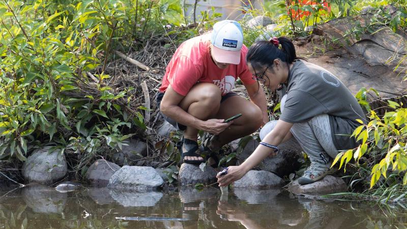 Student and faculty member participate in collaborative research and hands-on experiments collecting samples by a river