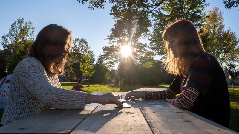Students play a game of cards on a picnic table.
