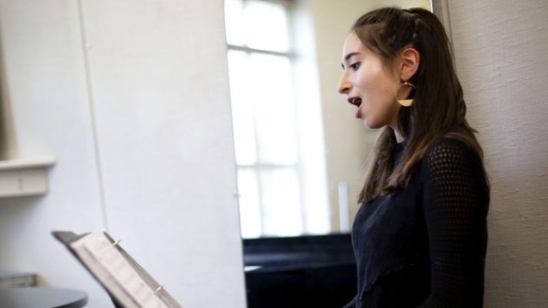 Emily Austin looks at sheet music on a music stand as she sings.