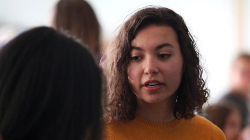 Sophie Dion-Kirschner, wearing a yellow sweater, speaks to a dark-haired girl.