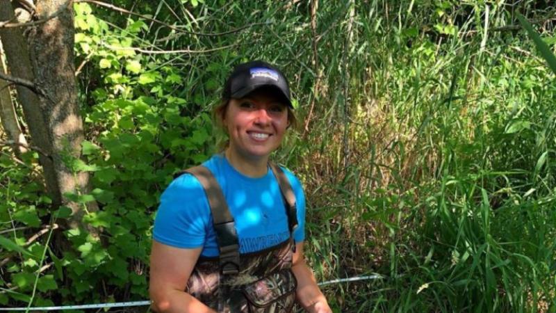Summer Kopitzke squats in a creek, surrounded by greenery.