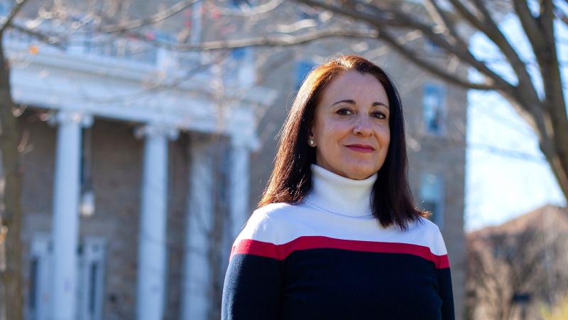 Rosa Tapia, wearing a black, red and white turtleneck, stands in front of Main Hall.
