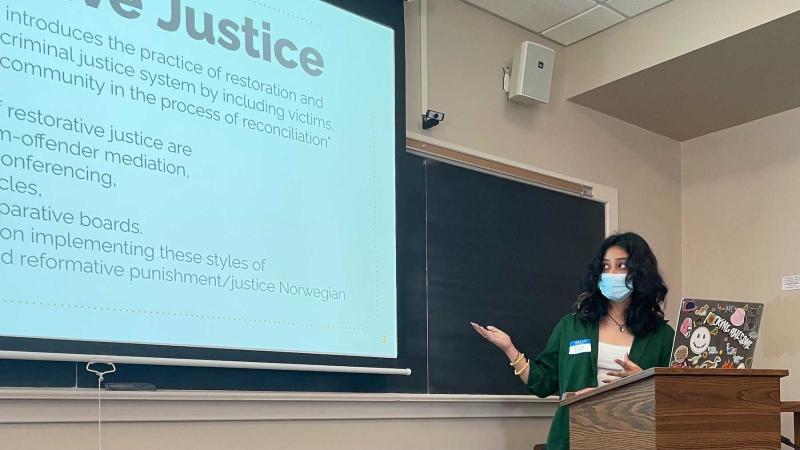 Tee Karki points to her work on a big screen during her Harrison Symposium presentation.