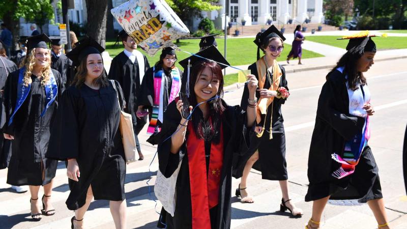 A graduate holds a Congrats Grad balloon as she and other graduates walk across 大学 Avenue during the 2022 Commencement.