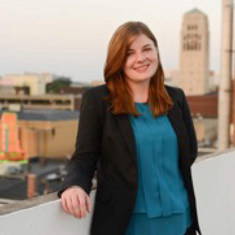 Person with hair past shoulders smiling looking into the camera leaning on a wall.  