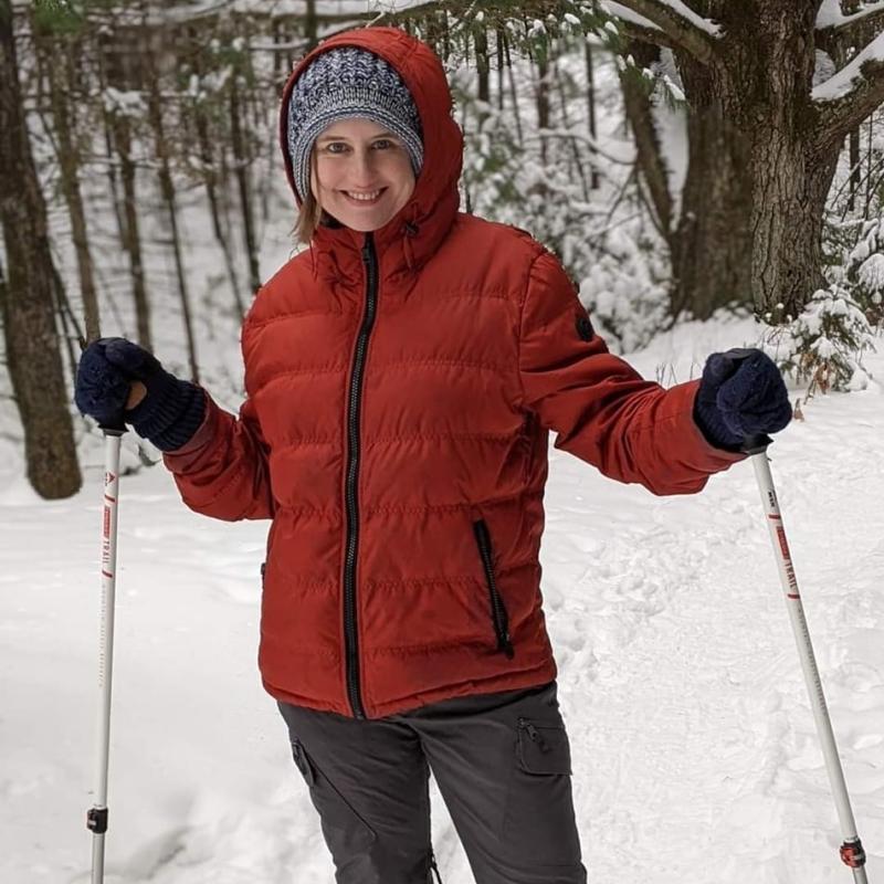 Celia, snowshoeing, in a rust-colored puffy coat and fuzzy hat.